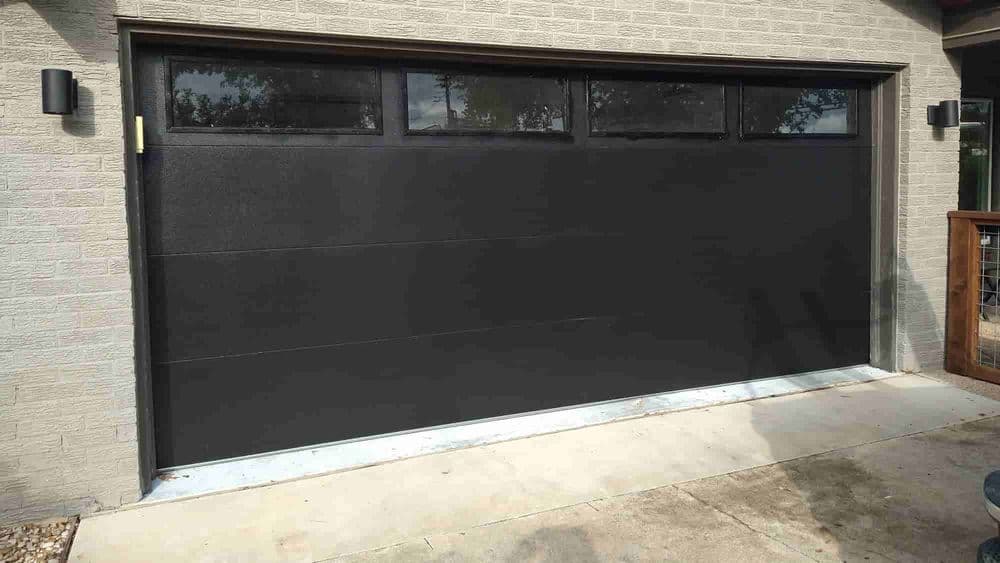 Modern black garage door with windows, installed on a contemporary home exterior.
