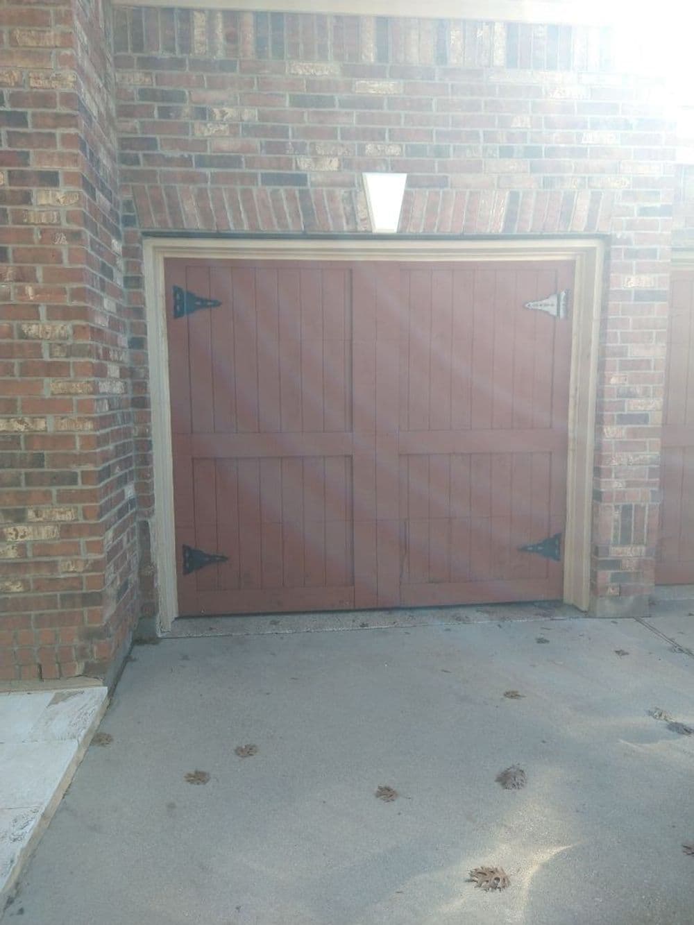 Wooden double garage doors with decorative hinges, set against a brick wall.