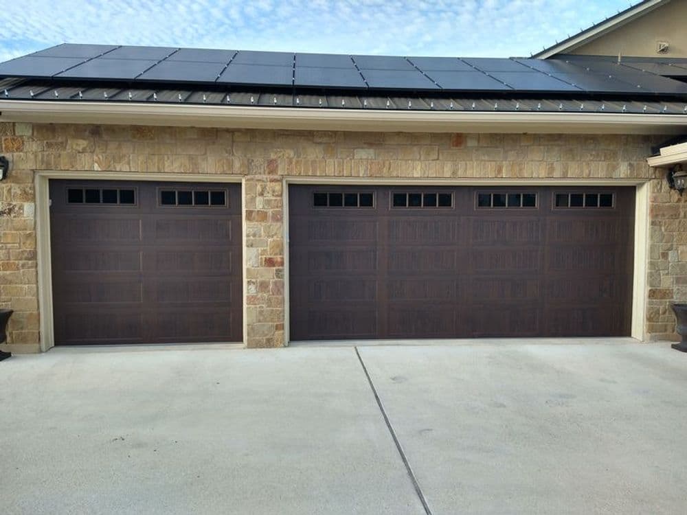 Modern garage doors with decorative windows on a stone home exterior, solar panels above.