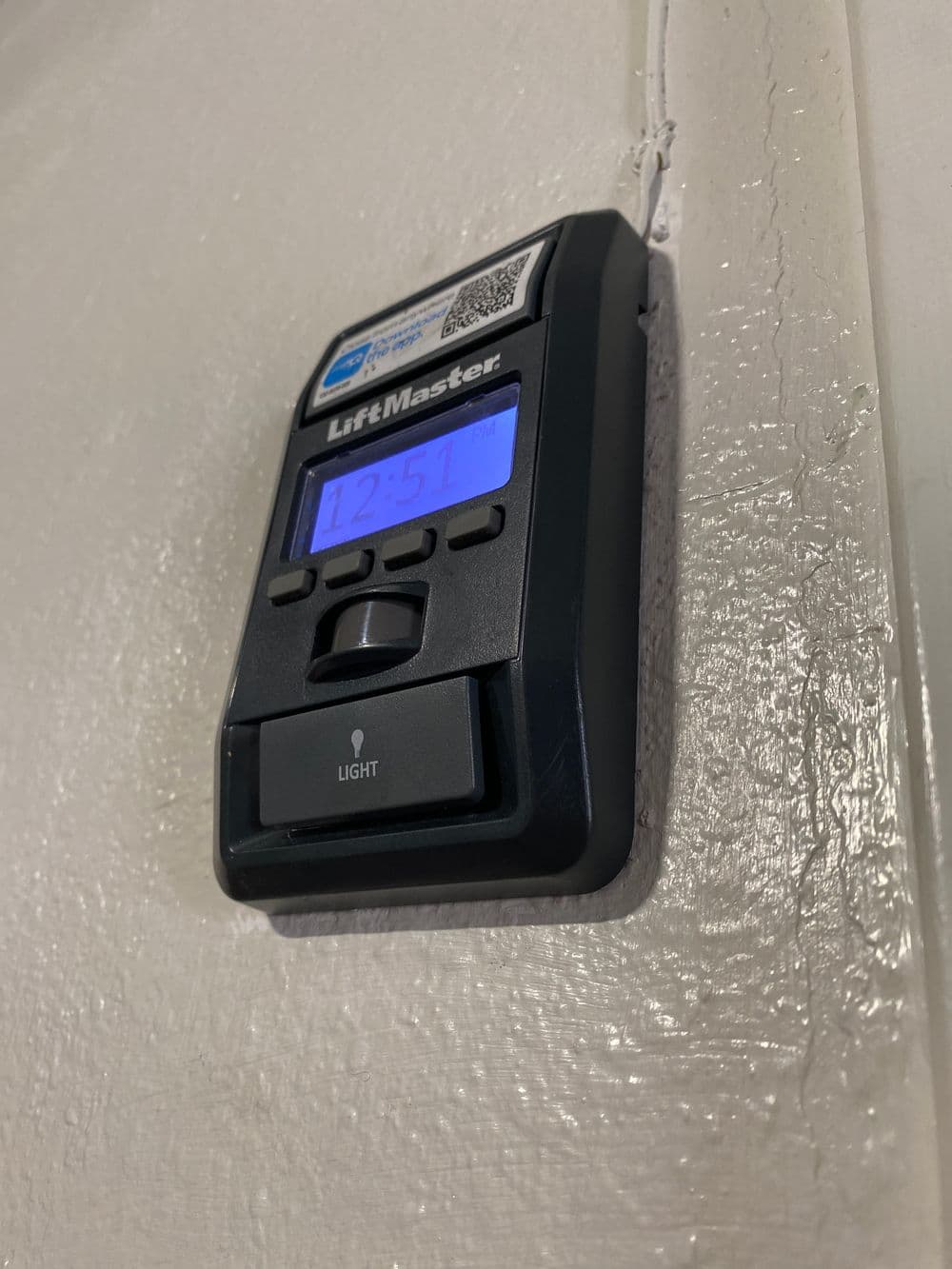 LiftMaster garage door remote with digital display mounted on a wall.