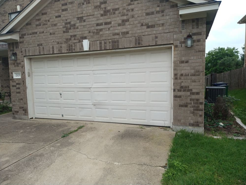 White garage door on a brick house with a concrete driveway and green grass.