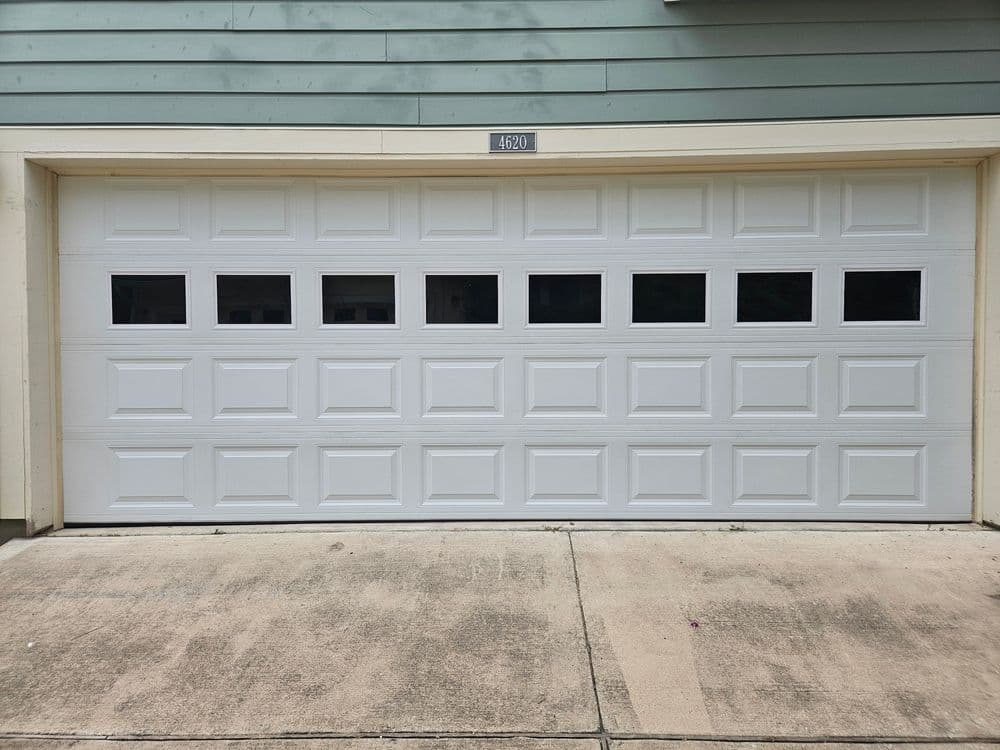 White garage door with multiple windows, installed on a light green house facade.