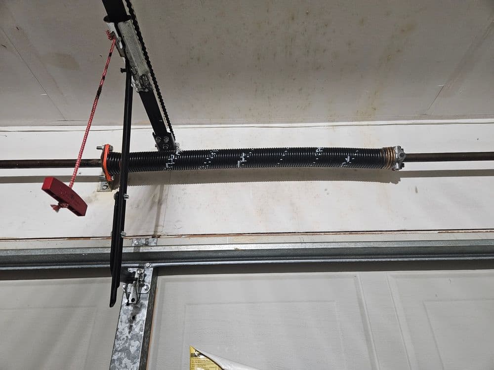Garage door torsion spring assembly and cable system mounted on a garage wall.
