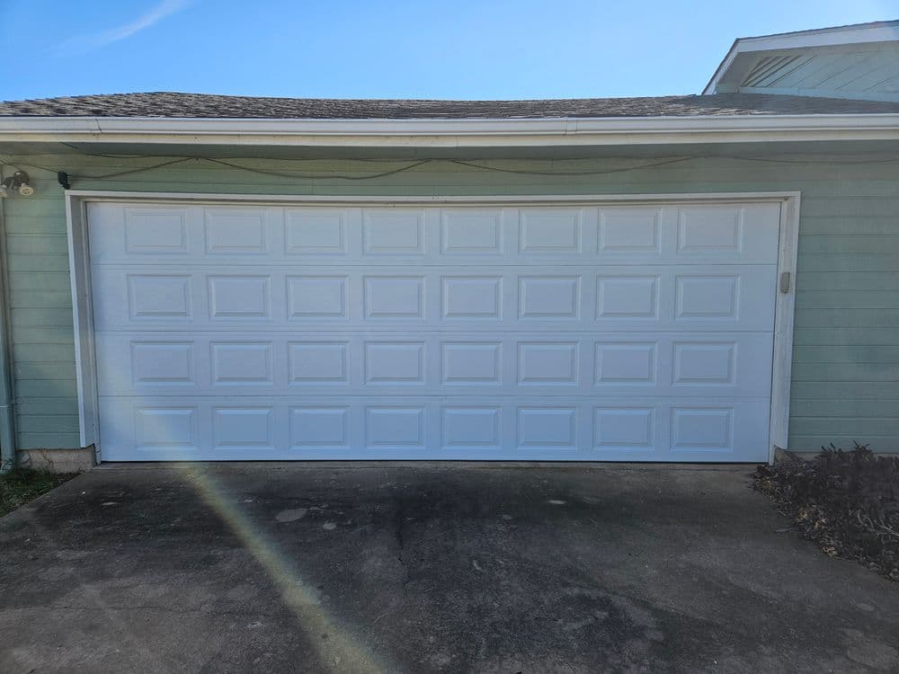 White garage door on a house with blue exterior and concrete driveway.
