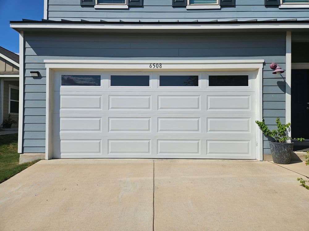 White garage door with window panels, modern home exterior, concrete driveway, and blue siding.