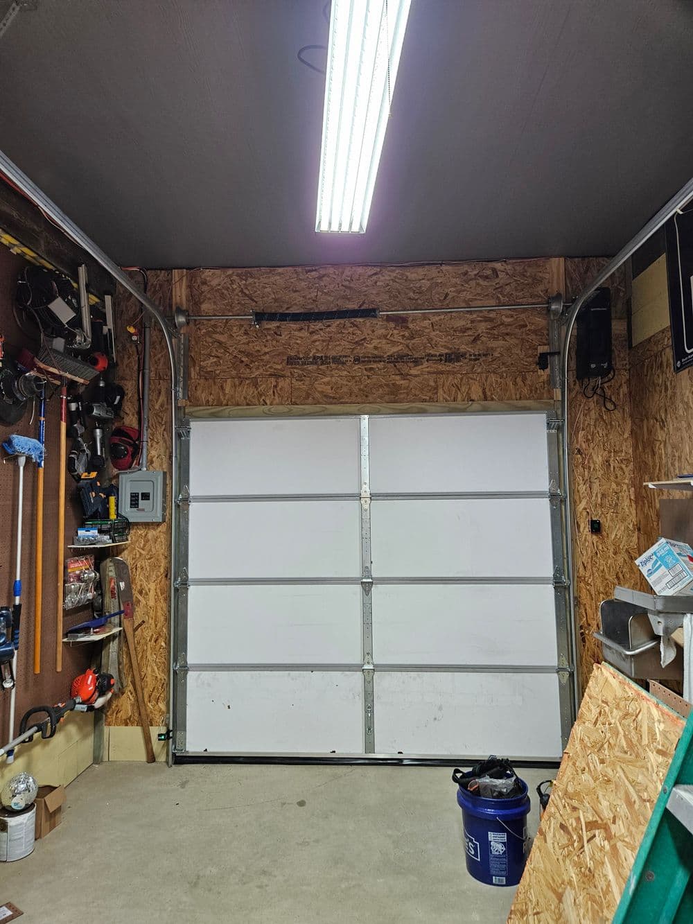Interior of a garage with a white door, tools on the wall, and bright overhead lighting.