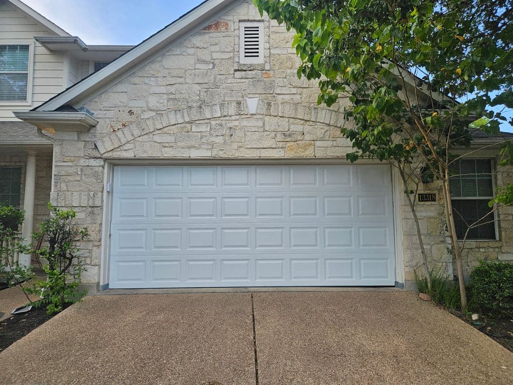 White garage door on a stone house exterior with landscaped front yard.